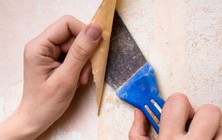 Hands removing old wallpaper using tools.