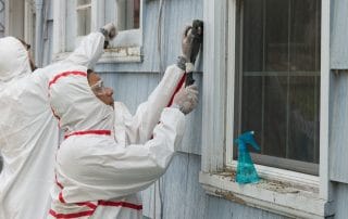 Two house painters in hazmat suits removing lead paint from an old house