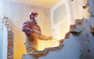 Man demolishing a wall in a home with sledgehammer