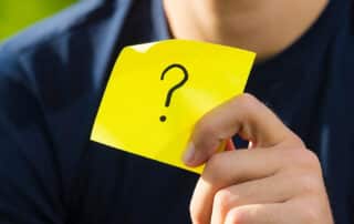Man holding up a sticky note with a question mark written on it